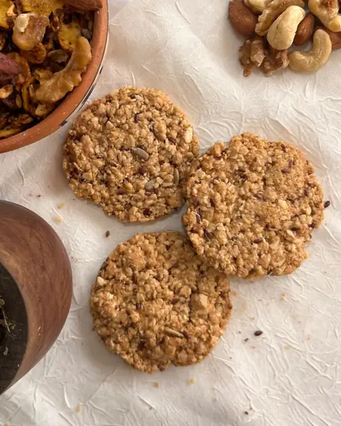 Tres galletitas de avena artesanales sobre papel, junto a un bowl de frutos secos y un mate