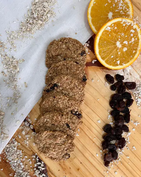 Galletitas con pasas de uva sobre una tabla, con pasas sueltas y media naranja