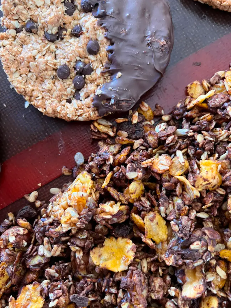 Granola bañada en chocolate junto a una galletita mitad cubierta de chocolate