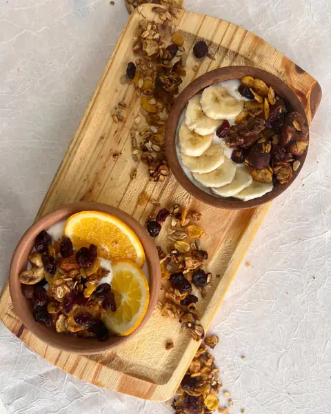 Dos bowls de granola con yogur, banana y rodajas de naranja sobre una tabla de madera